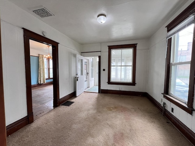 carpeted empty room with a wealth of natural light, a notable chandelier, and visible vents