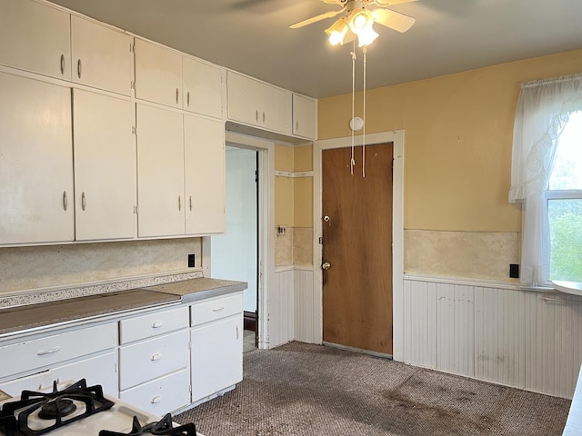 kitchen with wainscoting, dark carpet, light countertops, white cabinets, and a ceiling fan