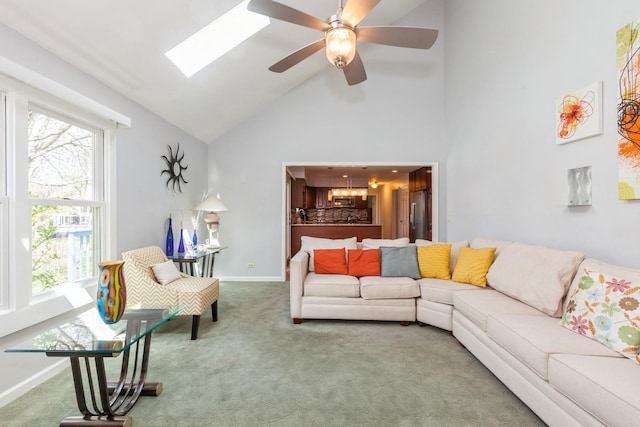carpeted living area with baseboards, ceiling fan with notable chandelier, a skylight, and high vaulted ceiling