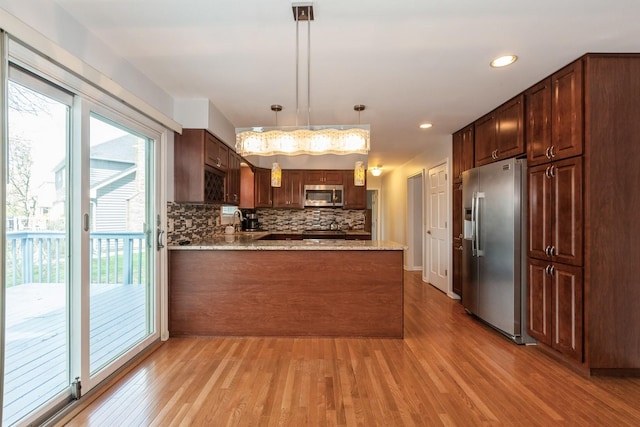 kitchen featuring a sink, light wood-style flooring, stainless steel appliances, a peninsula, and tasteful backsplash
