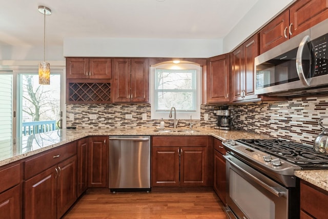 kitchen featuring backsplash, appliances with stainless steel finishes, hanging light fixtures, light stone countertops, and a sink