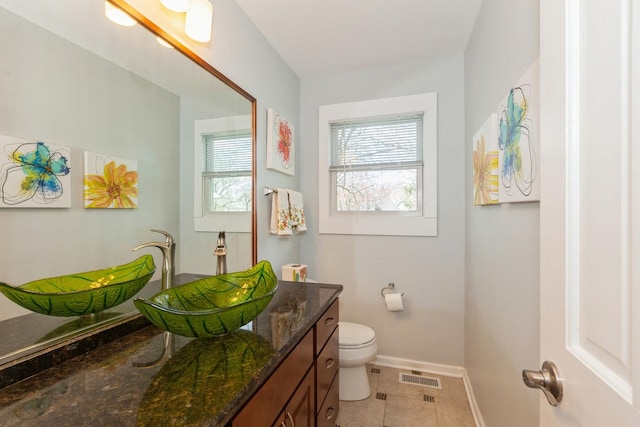 half bathroom featuring vanity, baseboards, a healthy amount of sunlight, and toilet