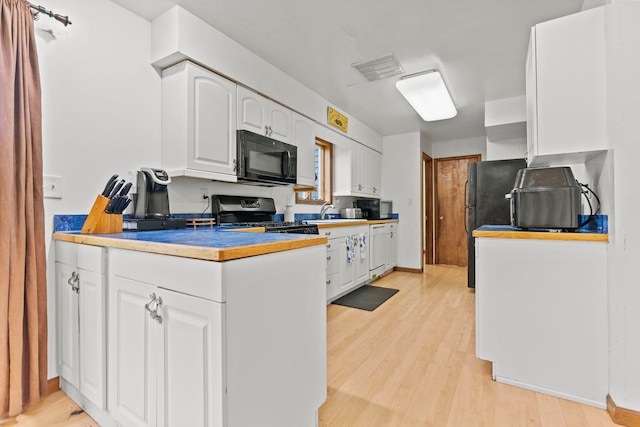 kitchen featuring white cabinets, black microwave, a sink, light wood-style floors, and stainless steel range with gas cooktop