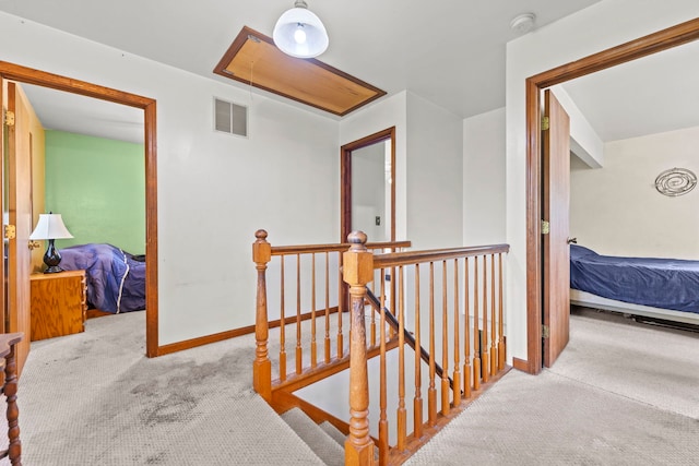 hall featuring visible vents, baseboards, attic access, carpet, and an upstairs landing
