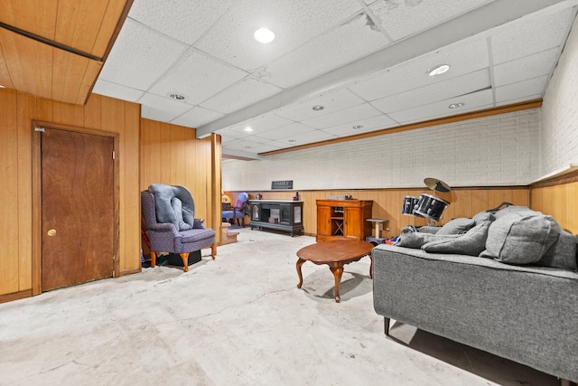 living room with concrete flooring, a drop ceiling, and wood walls