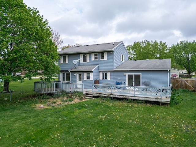 rear view of property featuring fence, a shingled roof, a lawn, and a deck