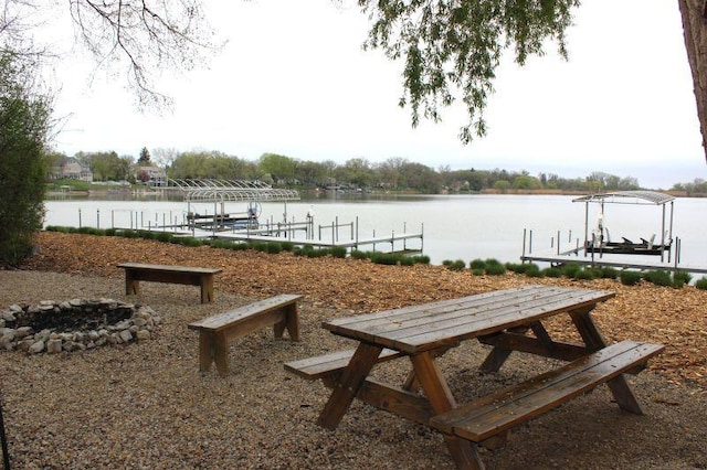 view of community with a boat dock, a water view, boat lift, and an outdoor fire pit