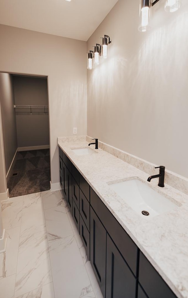 full bathroom with a sink, a walk in closet, baseboards, and double vanity