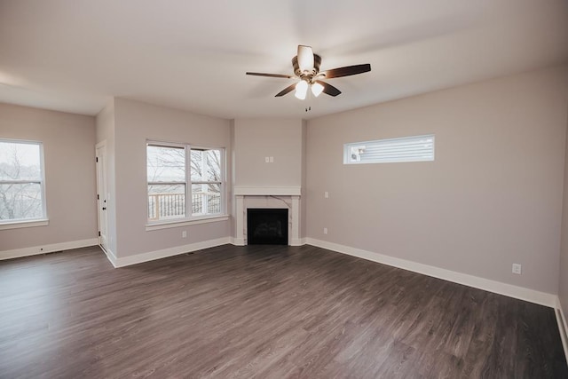 unfurnished living room with a high end fireplace, ceiling fan, dark wood-type flooring, and a wealth of natural light