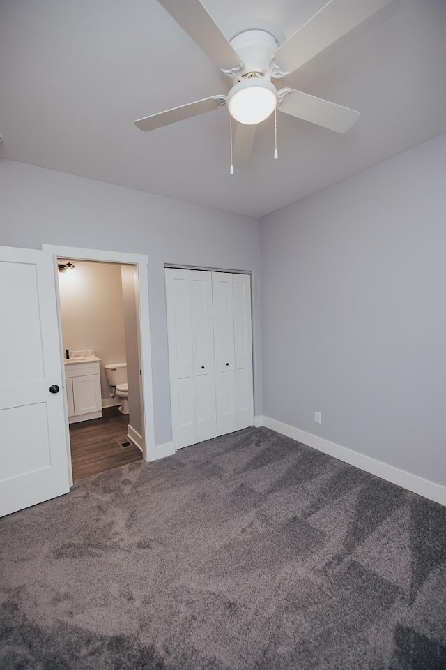 unfurnished bedroom featuring a closet, dark carpet, baseboards, ceiling fan, and ensuite bath