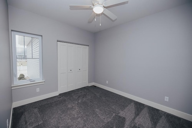 unfurnished bedroom featuring dark colored carpet, baseboards, ceiling fan, and a closet