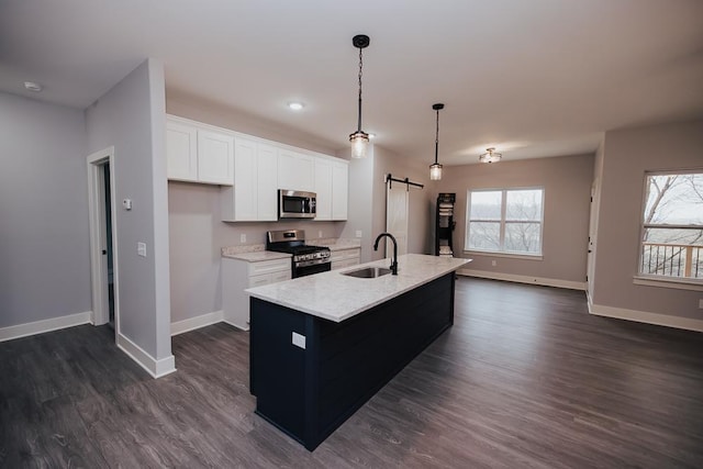 kitchen with appliances with stainless steel finishes, a barn door, a sink, baseboards, and dark wood-type flooring