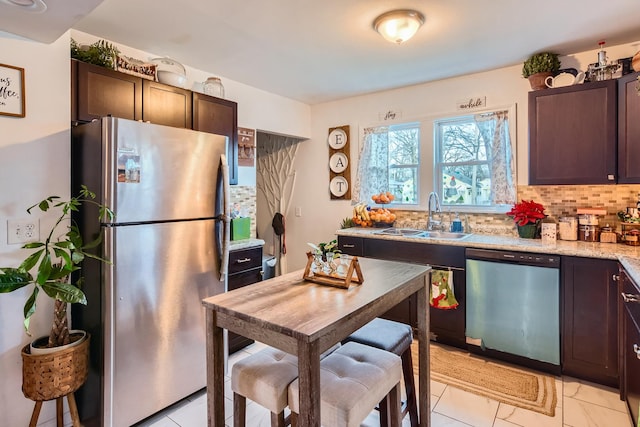 kitchen featuring dark brown cabinets, light stone countertops, a sink, stainless steel appliances, and decorative backsplash