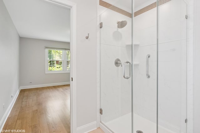 bathroom featuring wood finished floors, a shower stall, and baseboards