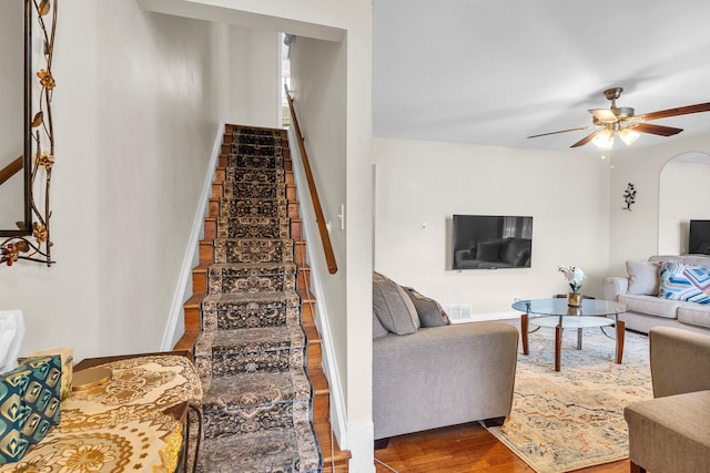 living room with stairs, wood finished floors, baseboards, arched walkways, and a ceiling fan