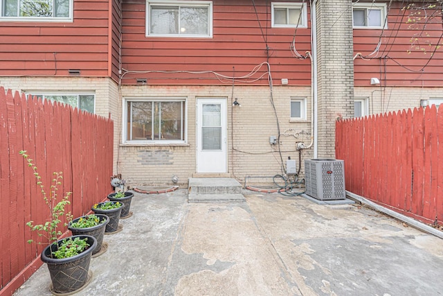 entrance to property featuring brick siding, fence, cooling unit, and a patio area