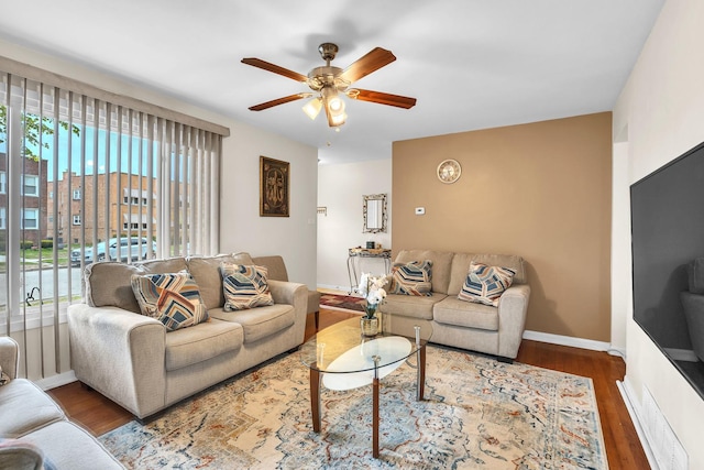 living area featuring baseboards, ceiling fan, wood finished floors, and a wealth of natural light