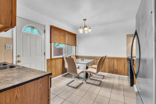 dining space featuring wood walls, an inviting chandelier, light tile patterned floors, and a wainscoted wall