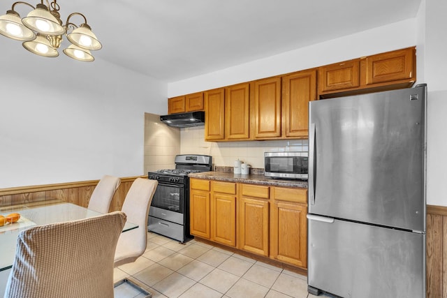 kitchen with decorative backsplash, dark countertops, under cabinet range hood, a notable chandelier, and stainless steel appliances