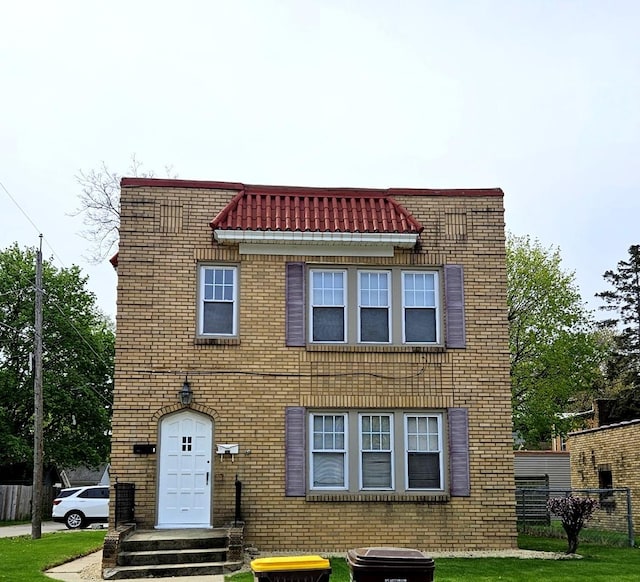 multi unit property with brick siding, a front lawn, and fence