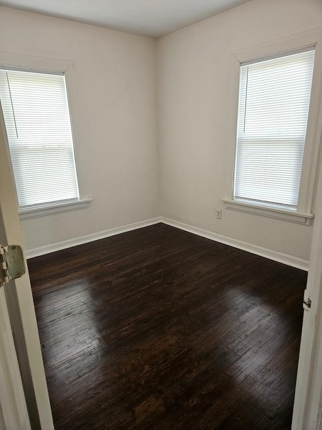 empty room featuring dark wood-style flooring, baseboards, and a wealth of natural light