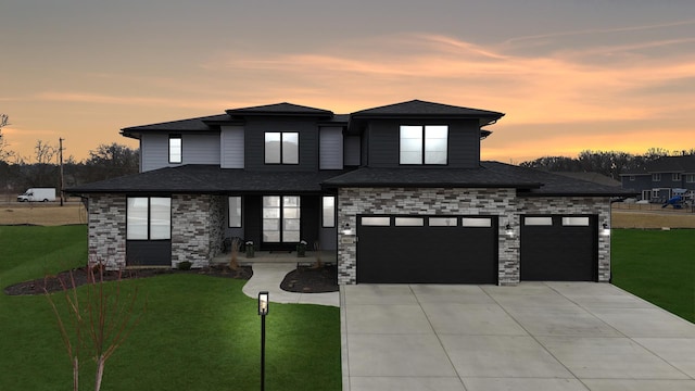 prairie-style house featuring roof with shingles, an attached garage, a yard, and driveway