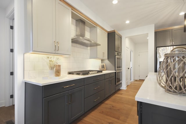 kitchen featuring light countertops, wall chimney exhaust hood, light wood finished floors, and stainless steel appliances