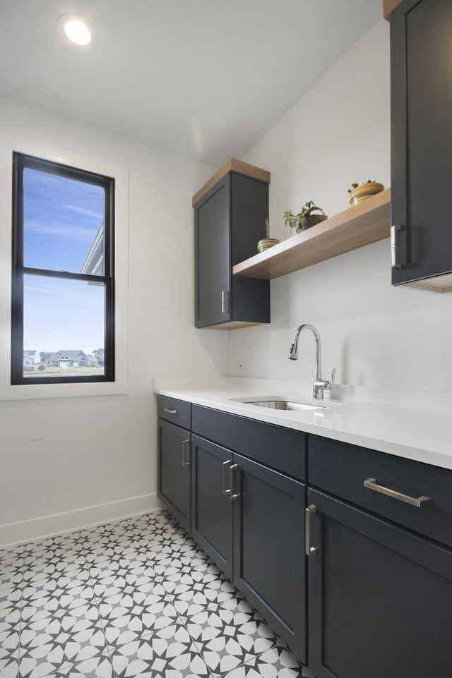 kitchen featuring a sink, baseboards, open shelves, and light countertops