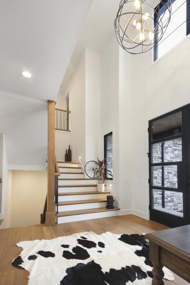 stairway featuring a notable chandelier, recessed lighting, baseboards, wood finished floors, and a towering ceiling