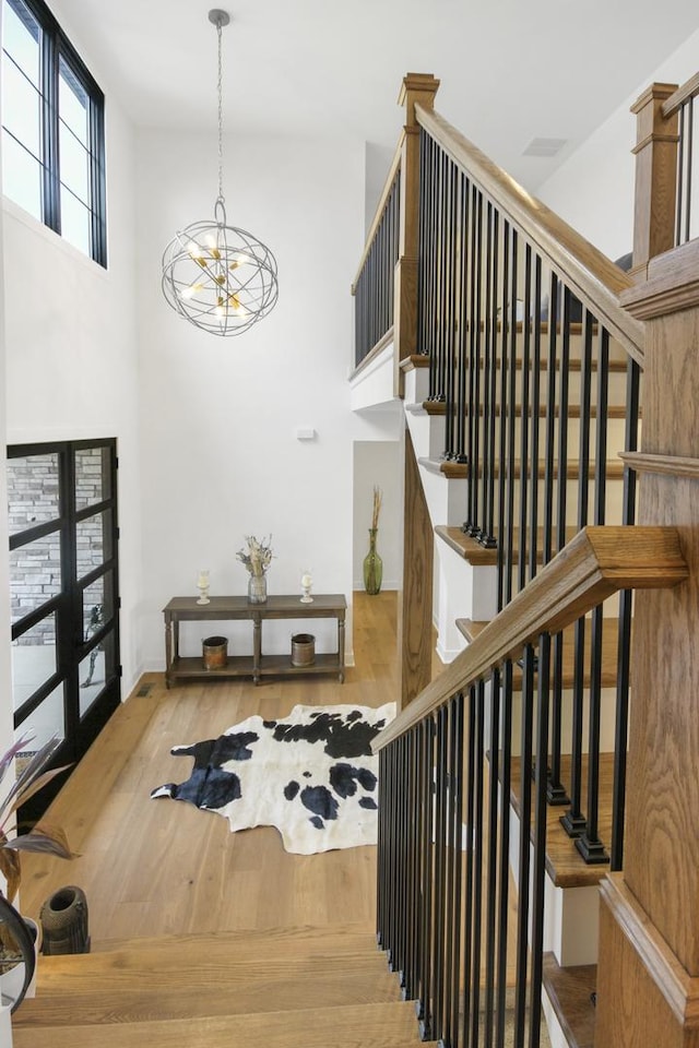 stairs with a towering ceiling, baseboards, wood finished floors, and a notable chandelier