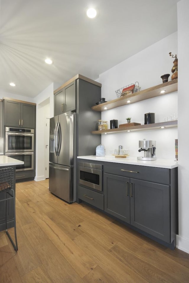 kitchen featuring appliances with stainless steel finishes, open shelves, wood finished floors, light countertops, and recessed lighting