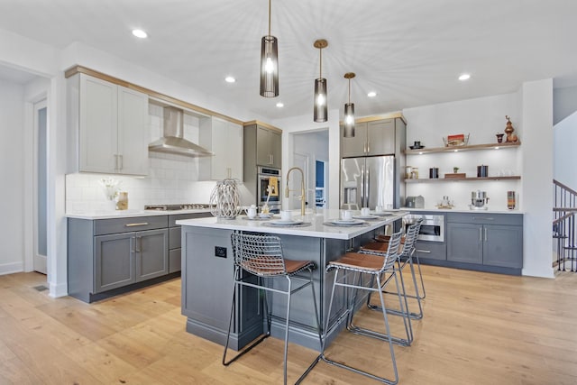kitchen featuring decorative backsplash, a breakfast bar, wall chimney range hood, gray cabinets, and appliances with stainless steel finishes