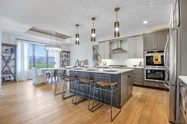 kitchen featuring gray cabinets, a kitchen bar, appliances with stainless steel finishes, light countertops, and a raised ceiling