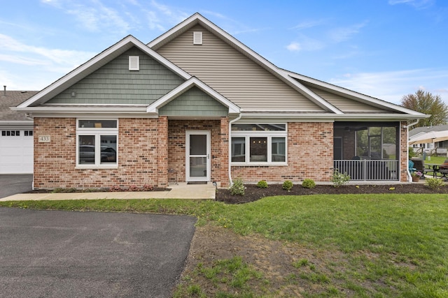 craftsman house featuring a garage, a front yard, brick siding, a sunroom, and driveway