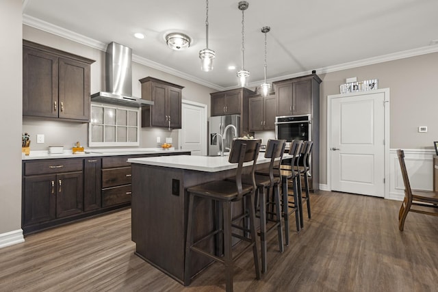 kitchen featuring dark brown cabinets, dark wood-style floors, a kitchen bar, wall chimney exhaust hood, and appliances with stainless steel finishes