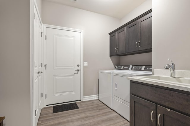 clothes washing area featuring a sink, washing machine and dryer, light wood-type flooring, and cabinet space