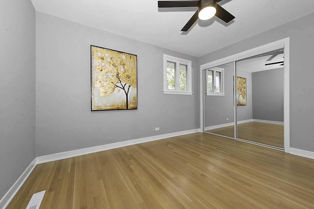 unfurnished bedroom with visible vents, a closet, wood finished floors, baseboards, and a ceiling fan