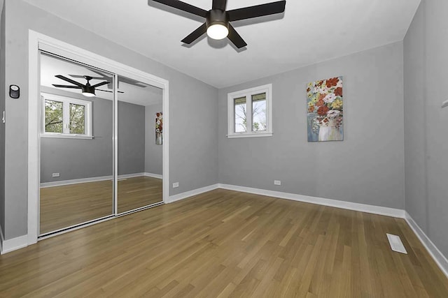 unfurnished bedroom with ceiling fan, baseboards, multiple windows, and wood finished floors