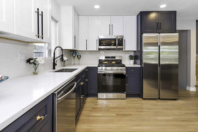 kitchen featuring appliances with stainless steel finishes, a sink, white cabinets, light wood finished floors, and recessed lighting
