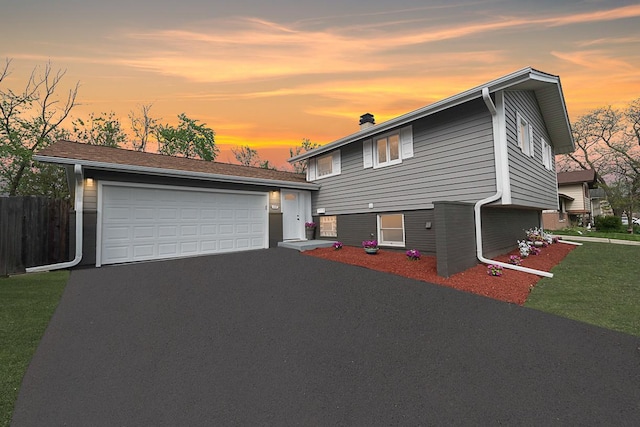 split level home with an attached garage, fence, driveway, and a chimney