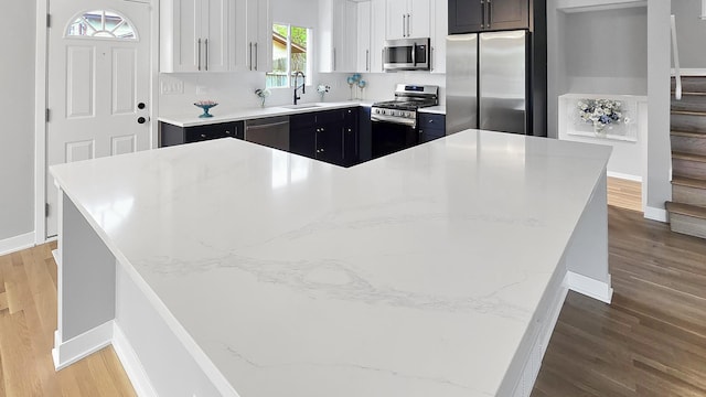 kitchen featuring appliances with stainless steel finishes, a sink, baseboards, wood finished floors, and a kitchen island