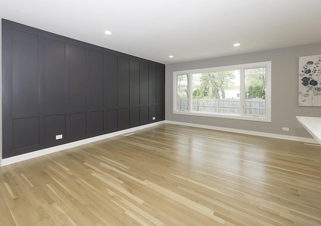 empty room featuring baseboards, recessed lighting, a decorative wall, and light wood-type flooring