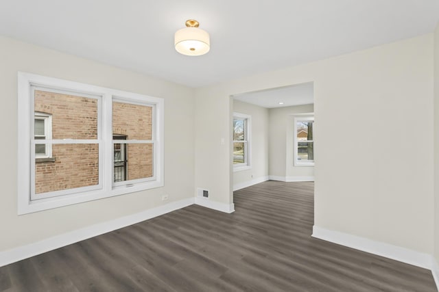 empty room featuring baseboards, dark wood-style flooring, and visible vents