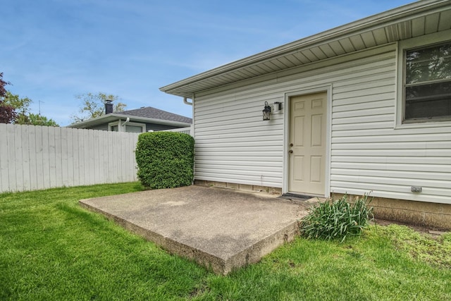 entrance to property featuring a patio area, fence, and a lawn