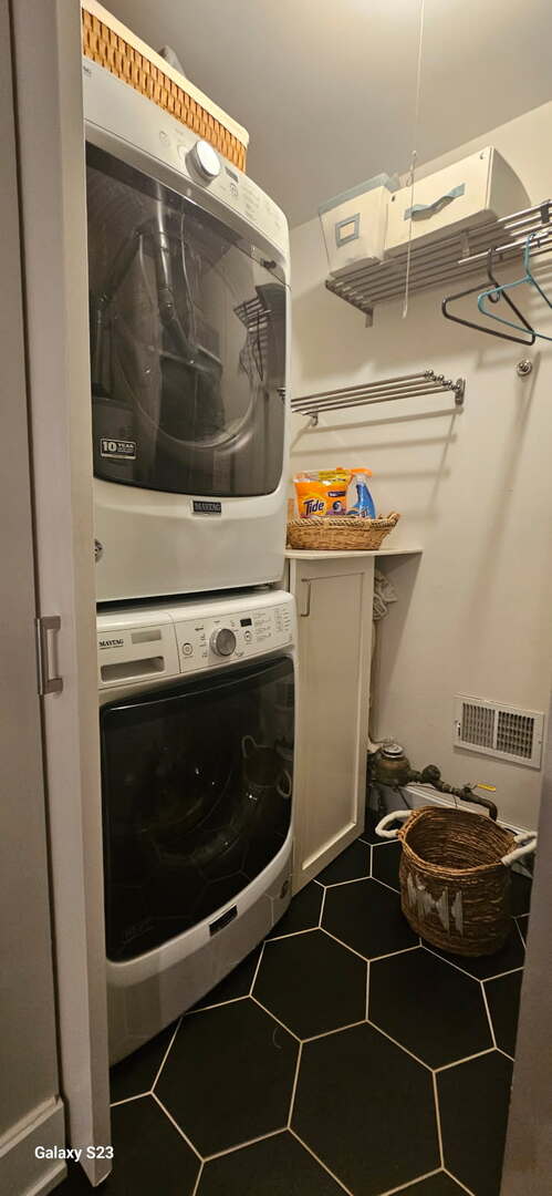 clothes washing area with stacked washer and clothes dryer, tile patterned floors, and cabinet space