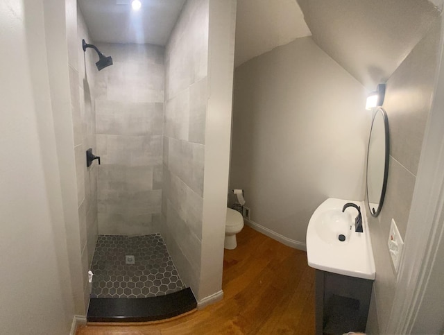full bathroom featuring a tile shower, wood finished floors, toilet, vanity, and lofted ceiling