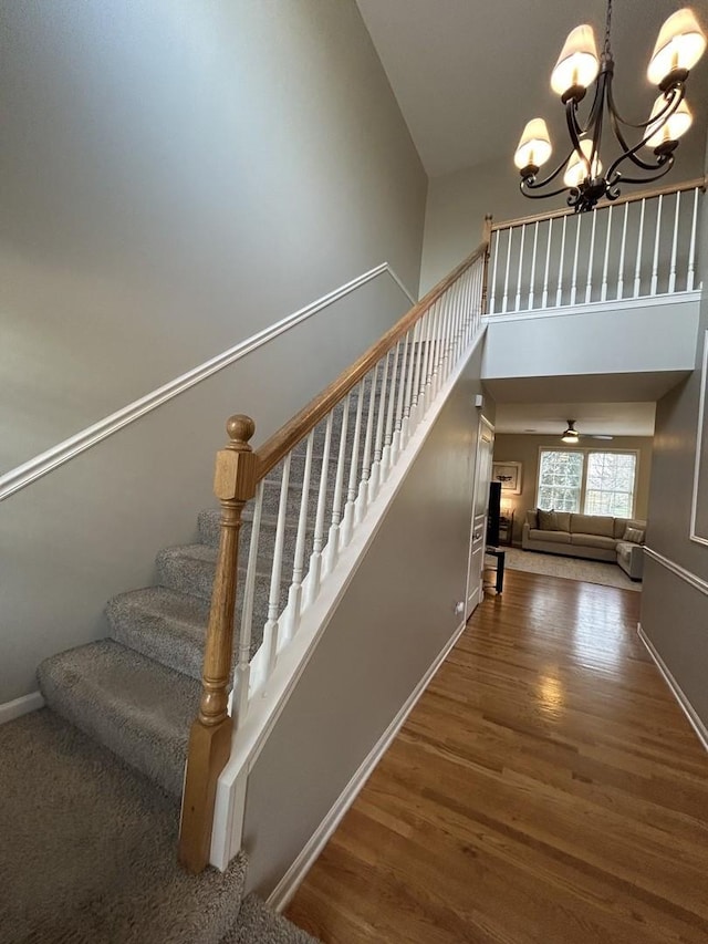 stairs with baseboards, a towering ceiling, wood finished floors, and a chandelier