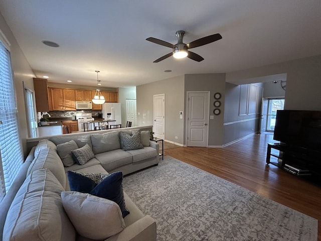 living area with baseboards, a ceiling fan, and dark wood finished floors