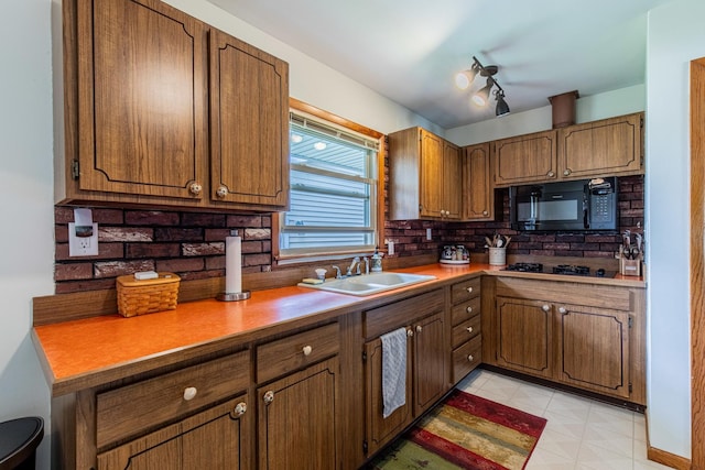 kitchen featuring a sink, light countertops, brown cabinetry, decorative backsplash, and black appliances