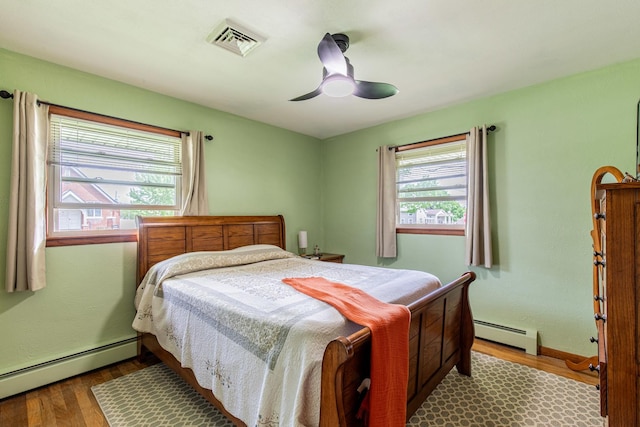 bedroom with baseboards, visible vents, wood finished floors, and a baseboard radiator
